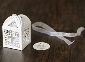 Detail of laser-cut cross gift box with white ribbon and thank you tag on wood
