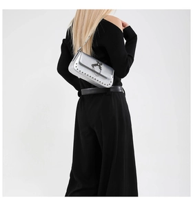 Detail of silver metallic shoulder bag featuring black cross charm and studded flap edge