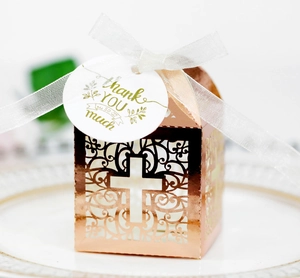Detail of rose gold laser-cut hollow cross candy box with white ribbon and thank you tag