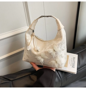 Détail de la broderie papillon 3D et texture dentelle sur un sac à main couleur crème