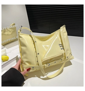 Close-up of light yellow patent leather shoulder bag with punk studs and zipper details