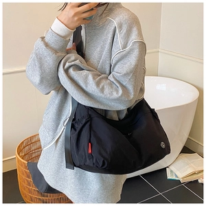 Close-up of black nylon crossbody bag with red label and smiley logo on casual model