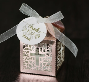 Detail of rose gold laser-cut cross favor box with silver ribbon and thank you tag