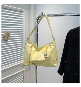 Close-up of a glossy yellow punk tote bag with studs and grommets on a metal hanger