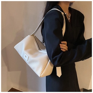 White pleated shoulder bag with vertical textures shown on model wearing black blazer