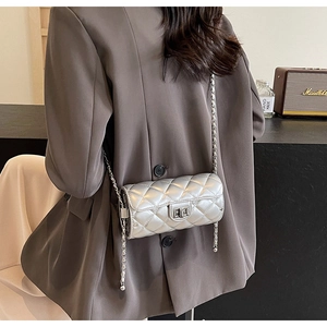 Silver quilted cylinder crossbody bag with metal chain strap worn by a model
