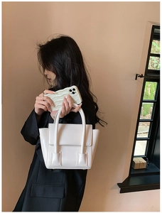Detail of a creamy white PU leather wing-style handbag held by a model in soft light