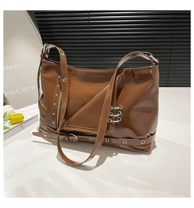 Detail of glossy brown leather shoulder bag with silver rivets and metal ring accents