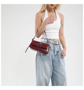 Detail of dark red punk crossbody bag featuring metal cross, chains, and silver studs