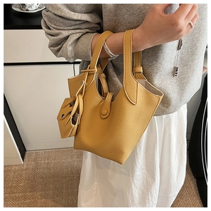 Detail of yellow bucket bag with lychee texture and matching mini pouch shown on a model
