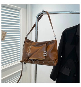 Detail of glossy brown crossbody bag with silver eyelets and decorative punk metal rings