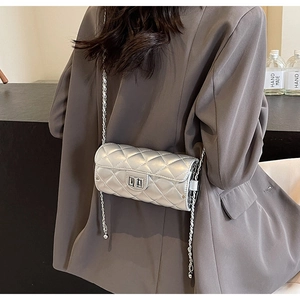 Sac argenté matelassé avec surpiqûres en losanges, chaîne et fermoir porté par un modèle