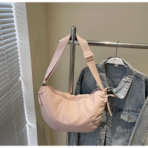 Pink crescent shoulder bag with pleated texture and adjustable strap hanging on rack