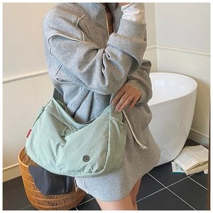 Light green nylon crossbody bag with drawstring detail and side red label shown in use