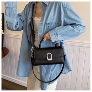 Detailed view of a black textured leather crossbody bag styled with a blue denim shirt