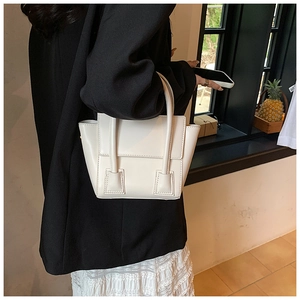 Detail of a creamy white trapezoid handbag with a fold-out side design and smooth texture