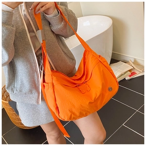 Detail of bright orange nylon crossbody bag with wide shoulder strap and metal logo