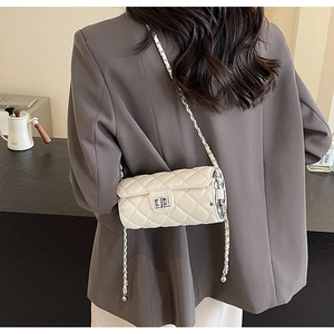 Vue arrière du mannequin portant un sac cylindre matelassé beige avec chaîne argentée en salle