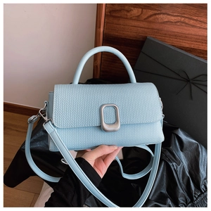 Close-up of light blue textured handbag with silver metal buckle and top handle detail