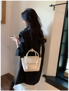 Close-up of a cream PU leather trapezoid handbag worn as a cross-body style by a model