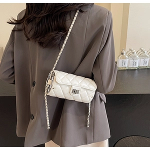 Detail of a beige quilted cylinder bag with silver twist lock and chain strap on model