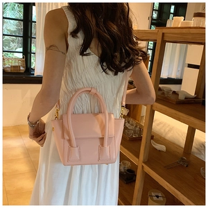 Model wearing a pink minimalist bucket bag with gold hardware in a cozy indoor setting