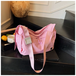 Detailed view of pink nylon crossbody bag with adjustable strap on wooden steps