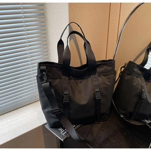 Detail of black tote bag featuring durable handles and adjustable buckle straps