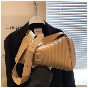 Detail of beige pleated handbag with wide strap and square buckle on dark blazer background