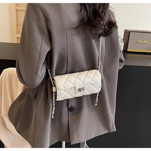 Close-up of white quilted leather chain bag worn over a brown blazer on model