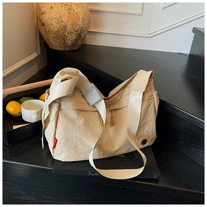 Macro view of beige nylon dumpling bag detailing a wide shoulder strap and plastic buckle