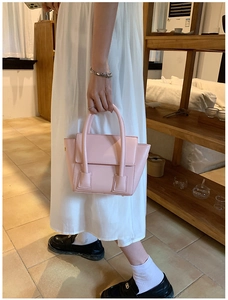 Detail view of a soft pink PU leather handbag with dual cylindrical handles and flap closure