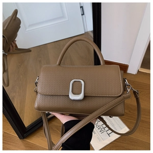 Detail of tan textured leather handbag with silver oval metal clasp and strap on wood floor