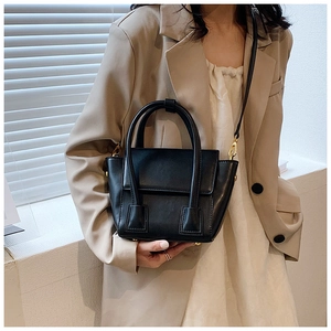 Detail of a black leather crossbody bag featuring gold hardware and curved handles
