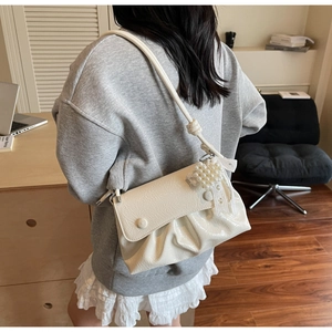 Sac à bandoulière plissé crème avec charm en perles porté par un mannequin en intérieur