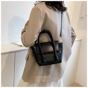 Detail of black matte PU leather crossbody bag with elegant gold hardware on model