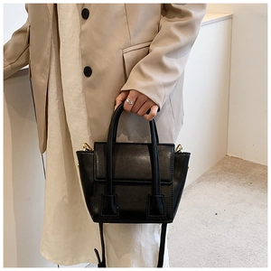 Detail of a black trapezoid faux leather handbag with gold hardware and dual handles