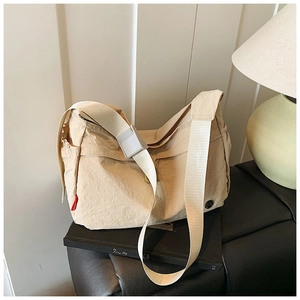 Detailed view of beige nylon dumpling bag showing adjustable strap and red side label