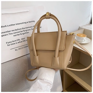 Detail of beige trapezoid PU handbag on a sofa with top handles and adjustable strap