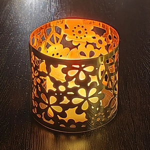 Hollow metal candle holder with floral patterns and warm LED light on wooden surface