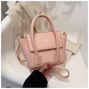 Pink faux leather trapezoid handbag with gold hardware displayed on a white chair