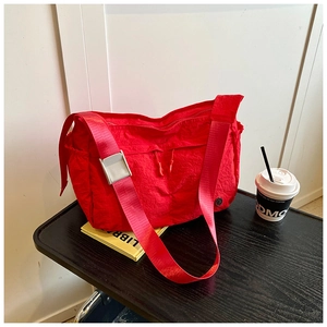 Detail of red nylon shoulder bag featuring wide strap with metal buckle and circular logo
