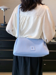 Light blue pleated crossbody pillow bag with square buckle shown on model shoulder