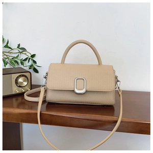 Detailed shot of beige lychee leather handbag with silver lock on a wooden desk