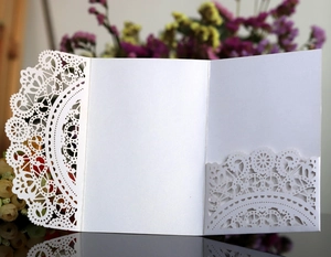 Macro detail of white laser-cut lace floral pattern on pearlescent wedding invitation card