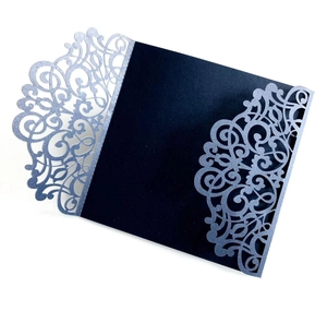 Close-up of dark blue wedding invitation featuring laser-cut floral patterns and glitter