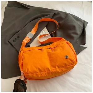 Macro view of bright orange nylon crossbody bag featuring dual front drawstring pockets
