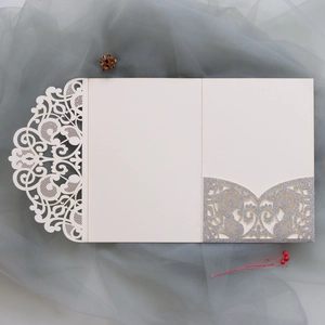 Detailed laser-cut wedding invitation card with intricate lace pattern and silver glitter pocket