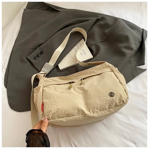 Detail of beige nylon messenger bag showing front zipper pockets and texture