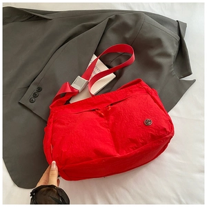 Detail of red nylon crossbody bag with circular metal logo on grey suit background
